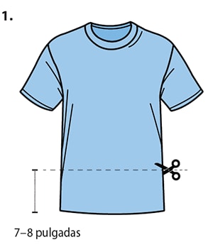 A front view of a T-shirt is shown. A straight, horizontal line is cut across the entire width of the T-shirt, parallel to the T-shirt’s waistline. Using a pair of scissors, the cut is made approximately seven to eight inches above the waistline. Both the front and back layer of the T-shirt are cut simultaneously.