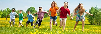 Group of smiling multiage children running outdoors holding hands.