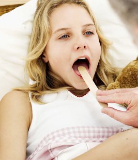 Close-up of a doctor putting a tongue depressor into the mouth of a girl.